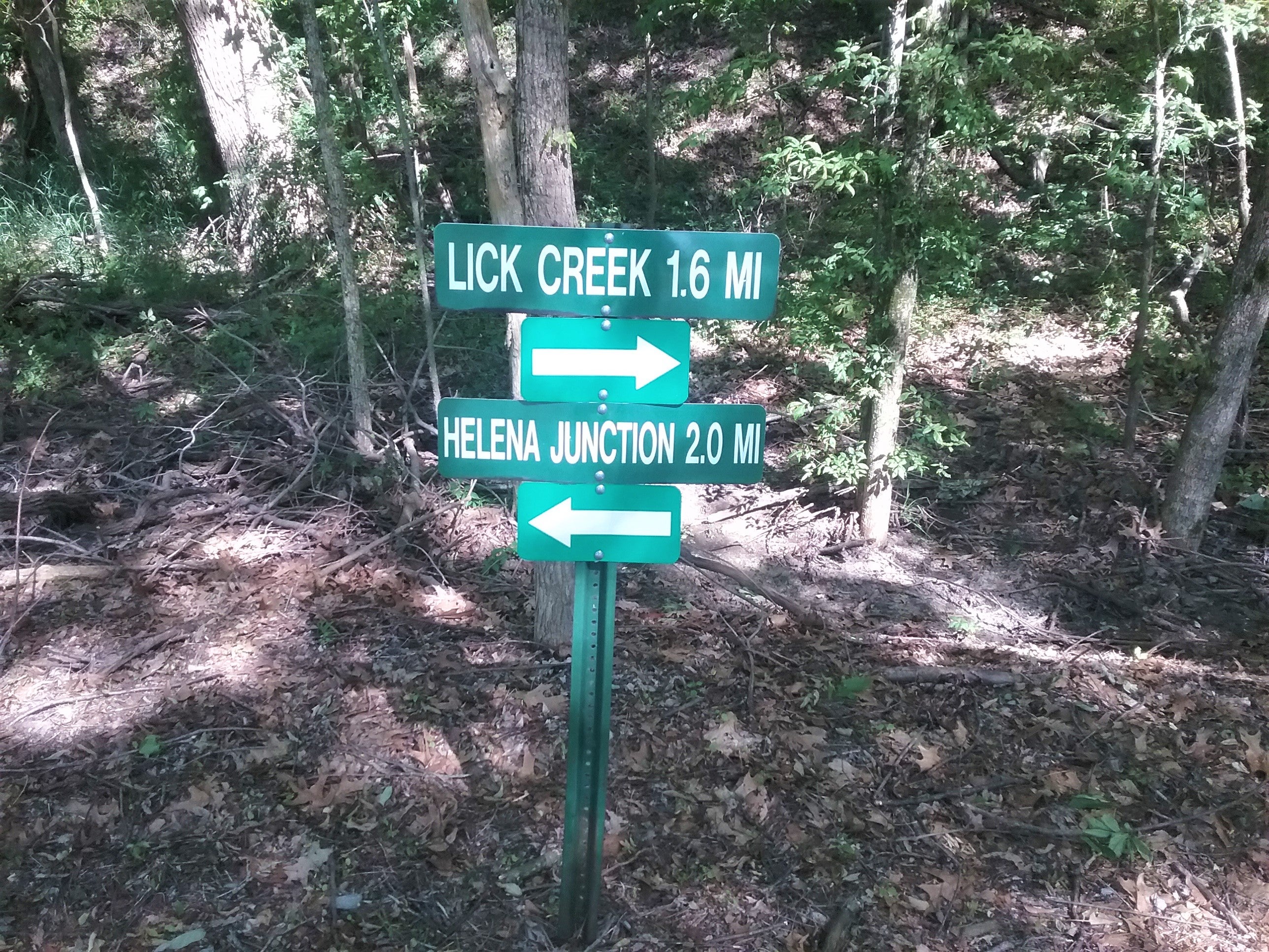 green signs on posts with arrows indicating Lick Creek to the south, 1.6 miles; Helena Junction to the north, 2 miles 